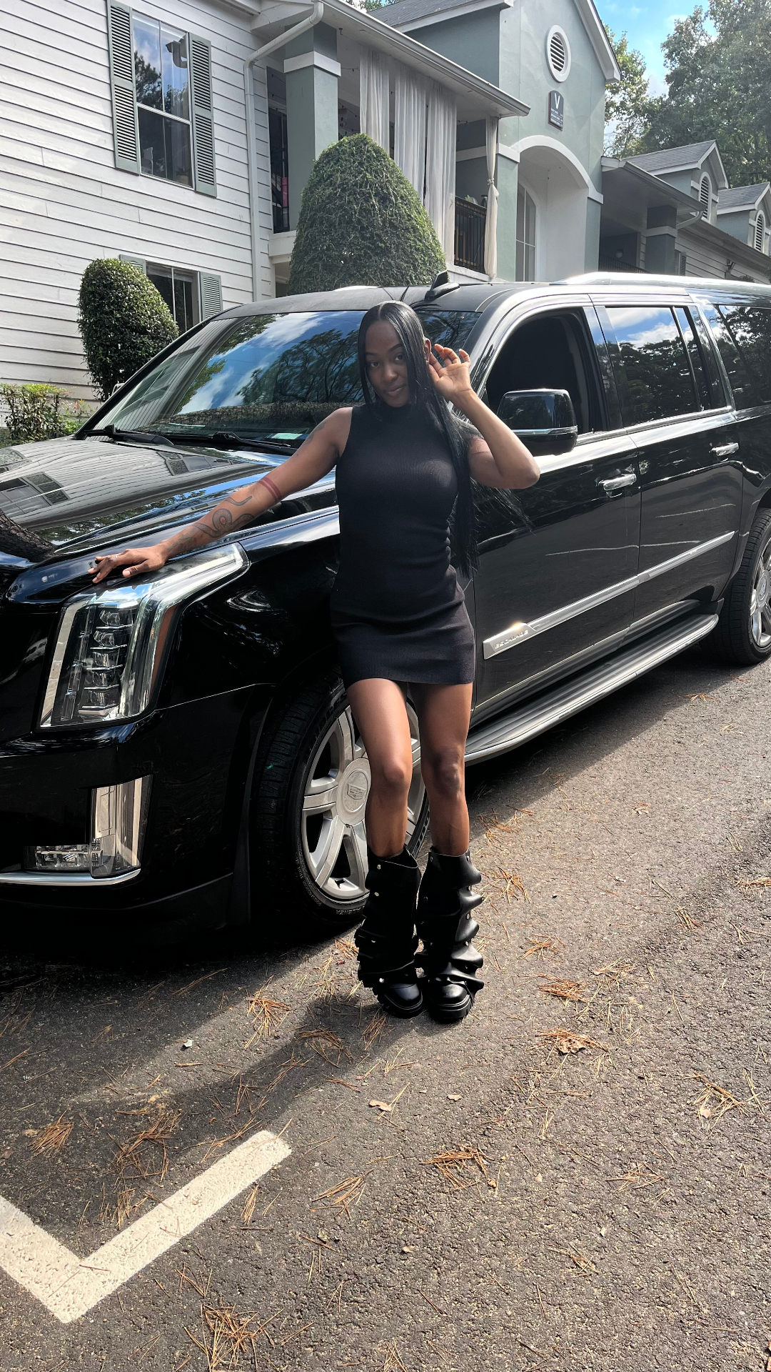@yammifr in a black dress leaning on the hood of the Escalade